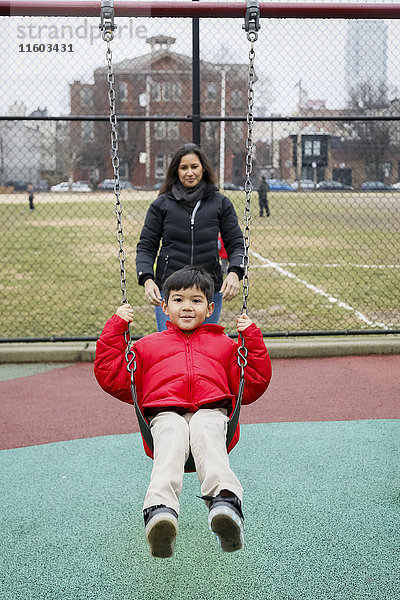 Mutter schiebt ihren Sohn auf dem Spielplatz auf die Schaukel