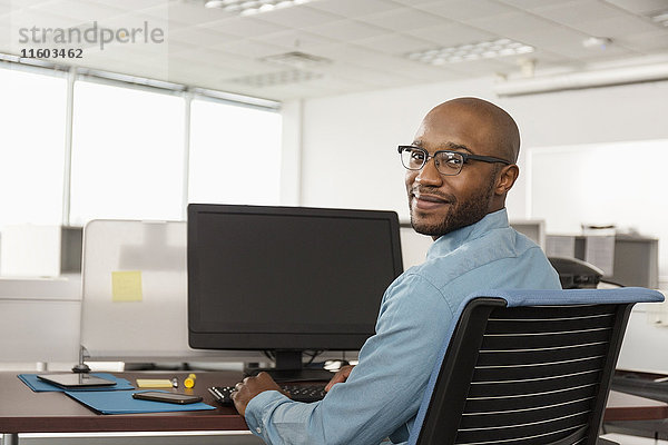 Lächelnder afroamerikanischer Mann am Computer im Büro