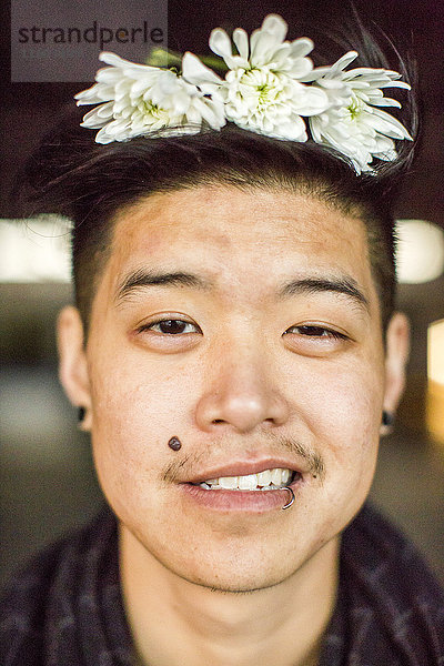 Porträt eines androgynen asiatischen Mannes mit Blumen im Haar