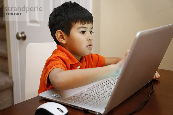 Amerikanischer Junge sitzt am Tisch und benutzt einen Laptop