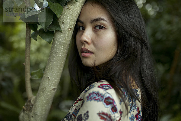 Porträt einer asiatischen Frau  die sich mit der Stirn auf einen Baumzweig stützt