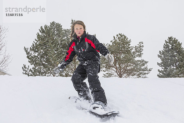 Ernstes Mädchen fährt Snowboard auf einem Hügel im Winter
