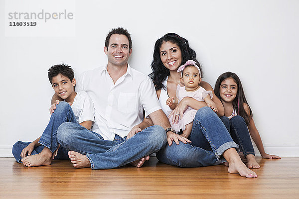 Porträt einer lächelnden gemischtrassigen Familie auf dem Boden sitzend