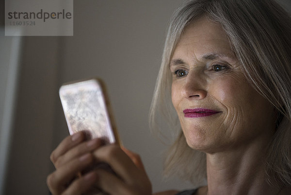 Lächelnde kaukasische Frau  die eine SMS auf ihrem Mobiltelefon schreibt