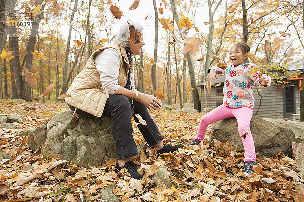 Großmutter und Enkelin spielen mit Herbstblättern