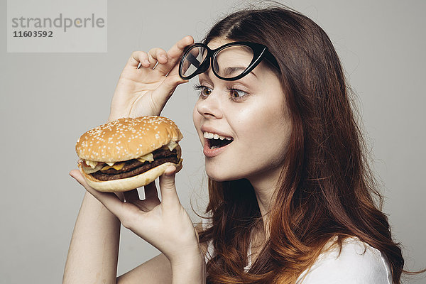 Kaukasische Frau hebt die Brille und betrachtet einen Cheeseburger