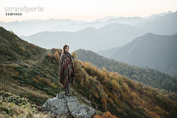 Kaukasische Frau steht auf einem Bergfelsen mit Blick auf ein Tal