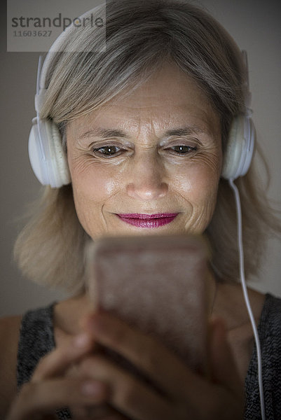 Lächelnde kaukasische Frau  die mit ihrem Mobiltelefon Musik hört