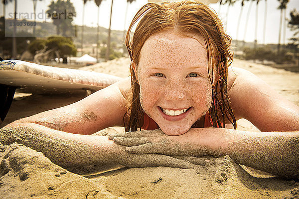 Porträt eines lächelnden Mädchens  das am Strand liegt und mit Sand bedeckt ist