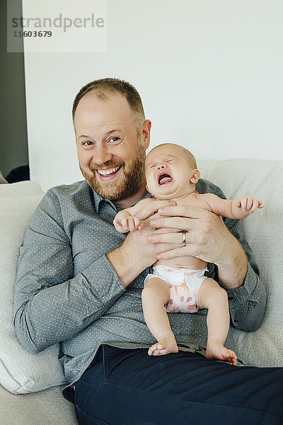 Porträt eines lächelnden Vaters  der seine weinende kleine Tochter hält