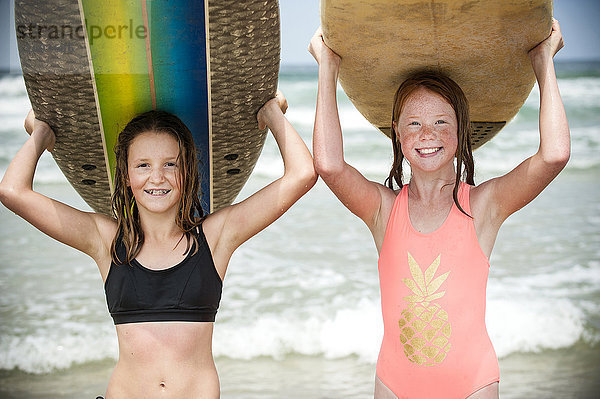 Porträt von lächelnden Mädchen  die Surfbretter auf ihren Köpfen balancieren