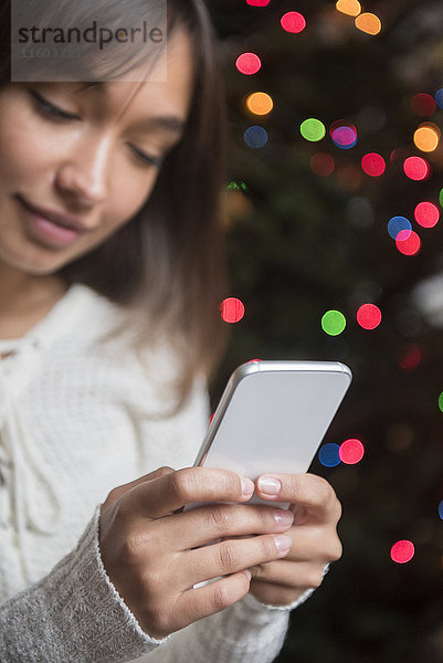 Gemischtrassige Frau  die in der Nähe des Weihnachtsbaums mit ihrem Handy telefoniert