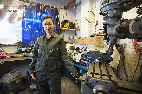 Mixed Race Frau posiert in der Nähe von Maschinen in der Werkstatt