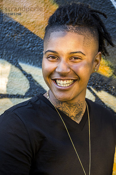 Porträt einer androgynen gemischtrassigen Frau  die in der Nähe einer Graffiti-Wand lächelt