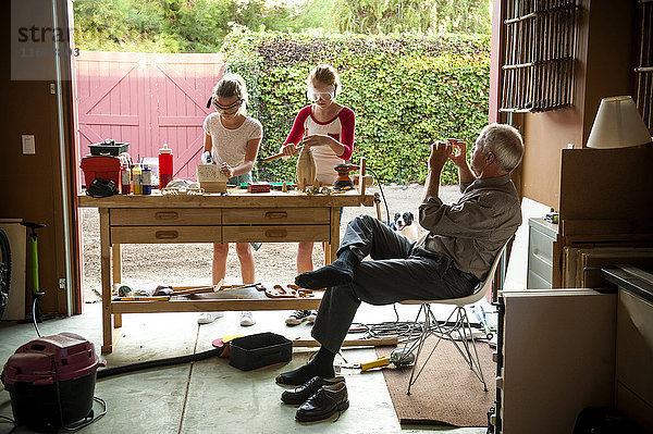 Großvater fotografiert seine Enkelinnen beim Bau eines Vogelhauses in der Garage