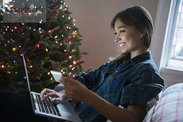 Mixed-Race-Frau beim Online-Shopping mit Laptop in der Nähe des Weihnachtsbaums