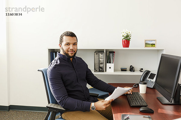 Mixed Race Mann liest Papierkram in der Nähe von Computer im Büro