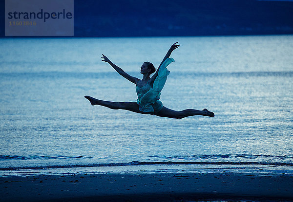 Kaukasische Ballerina springt bei Sonnenuntergang am Strand