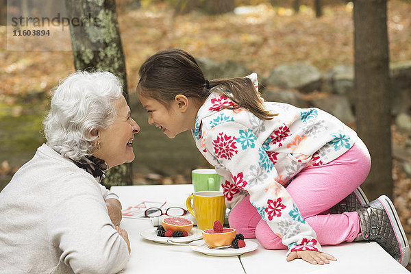 Großmutter und Enkelin spielen am Frühstückstisch im Freien