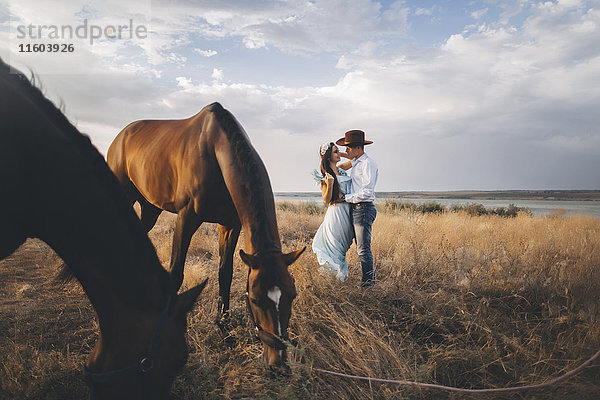 Weidende Pferde in der Nähe einer kaukasischen Frau  die einen Cowboy umarmt