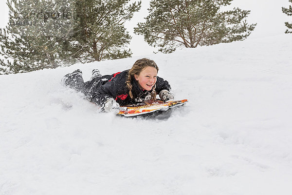 Lächelndes Mädchen gleitet auf dem Snowboard auf einem Hügel im Winter