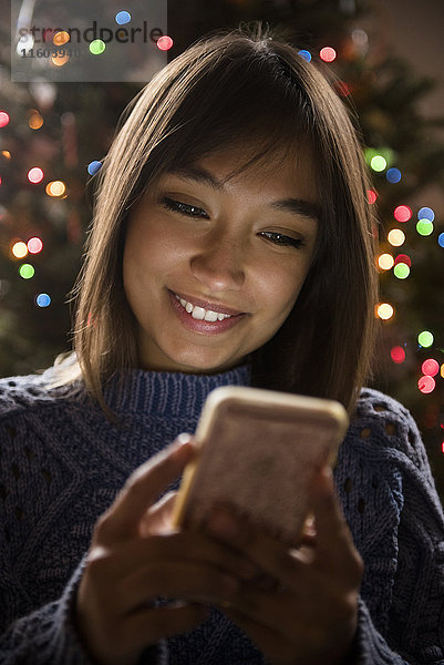 Gemischtrassige Frau  die in der Nähe des Weihnachtsbaums mit ihrem Handy telefoniert