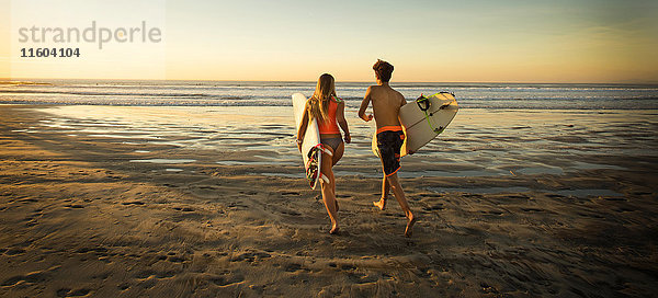 Teenager und Mädchen mit Surfbrettern laufen zum Meer