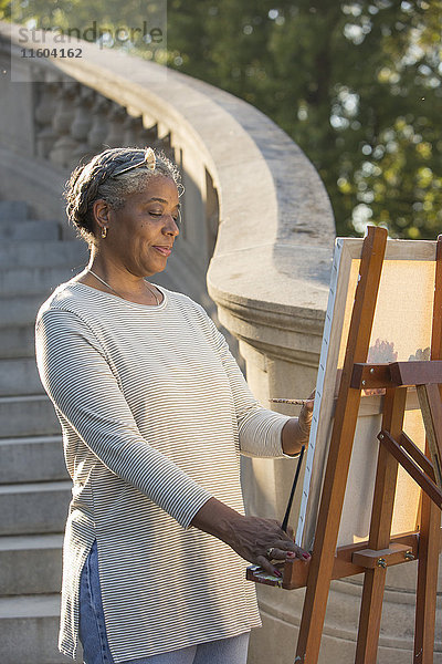 Schwarze Frau malt auf Leinwand in der Nähe einer Steintreppe