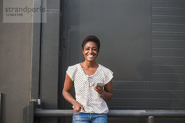 Lächelnde afroamerikanische Frau lehnt sich an ein Geländer und schreibt eine SMS auf ihrem Handy
