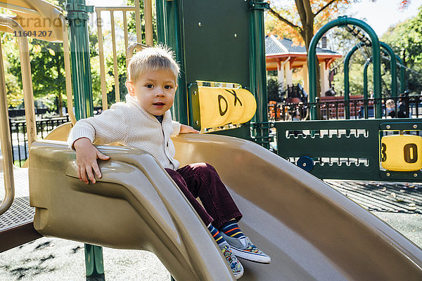 Porträt eines gemischtrassigen Jungen  der auf einer Spielplatzrutsche sitzt