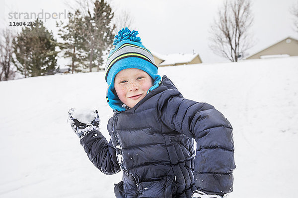 Lächelnder Junge wirft Schneeball im Winter