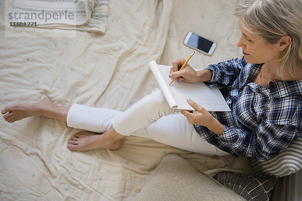 Kaukasische Frau sitzt auf dem Bett und schreibt auf einem Handy