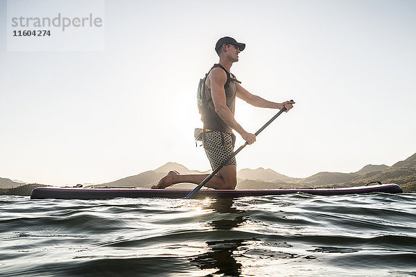 Kaukasischer Mann kniend auf Paddleboard im Fluss