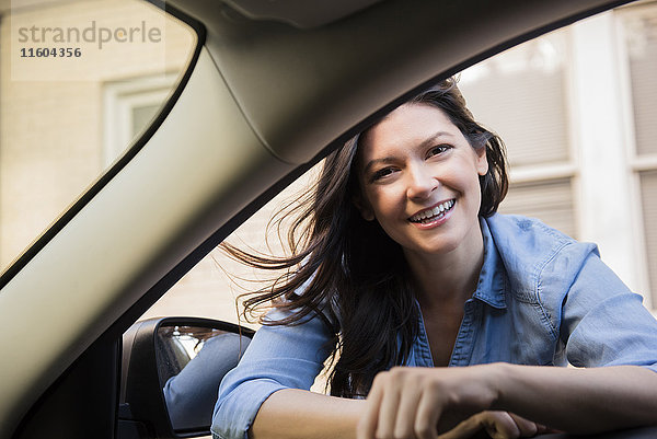 Lächelnde kaukasische Frau  die sich in ein Autofenster lehnt
