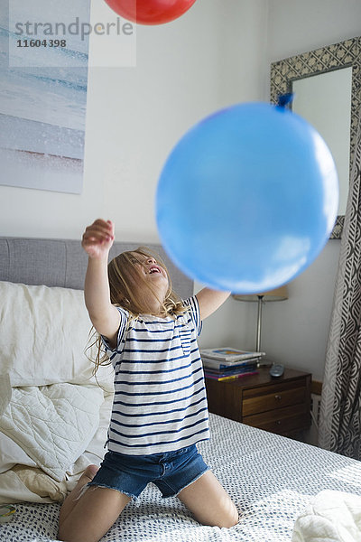 Kaukasisches Mädchen kniet auf dem Bett und spielt mit Luftballons