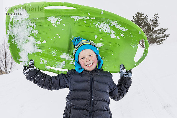 Lächelnder Junge posiert mit Schlitten im Winter