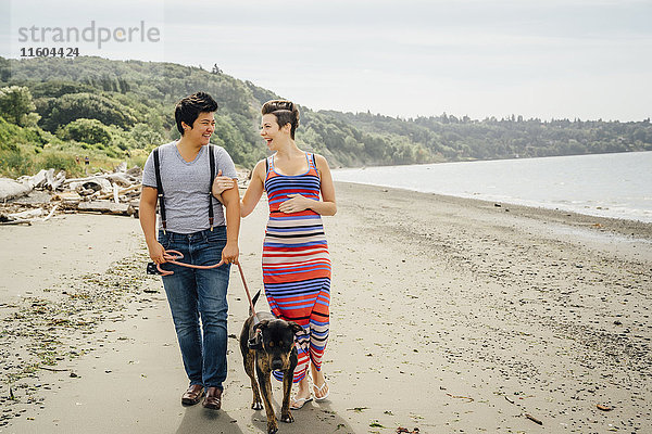 Schwangeres lesbisches Paar geht mit Hund am Strand spazieren