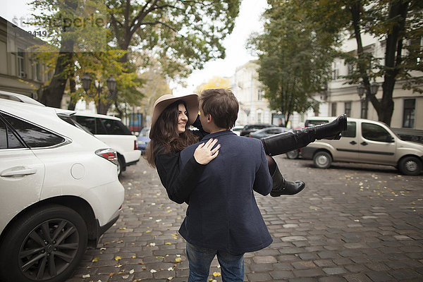 Kaukasischer Mann trägt Frau auf einer Kopfsteinpflasterstraße