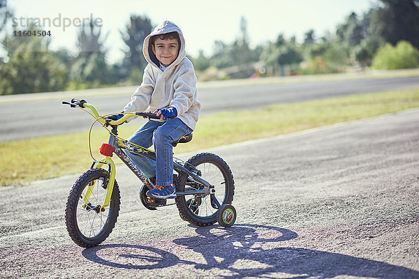 Hispanischer Junge posiert auf einem Fahrrad mit Stützrädern