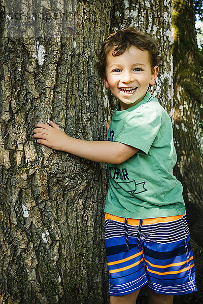 Porträt eines lächelnden kaukasischen Jungen  der einen Baum umarmt