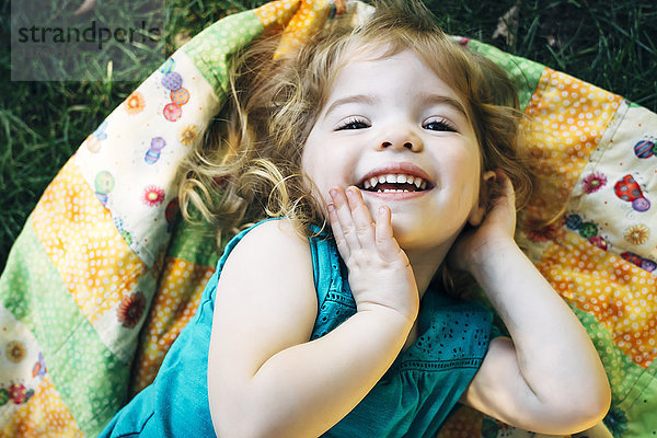 Porträt eines lächelnden kaukasischen Mädchens im Vorschulalter  das auf einer Decke im Freien liegt