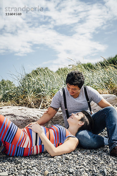 Schwangeres lesbisches Paar entspannt sich am felsigen Strand