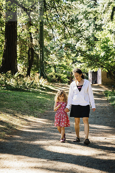 Kaukasische Mutter und Tochter gehen auf einem Weg im Park spazieren