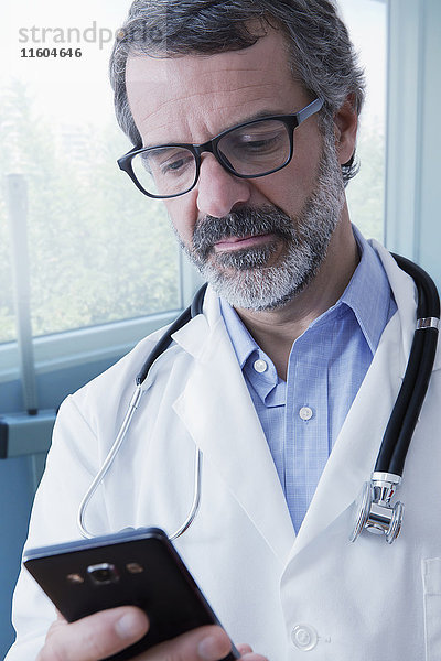 Hispanischer Arzt  der eine SMS auf seinem Mobiltelefon schreibt