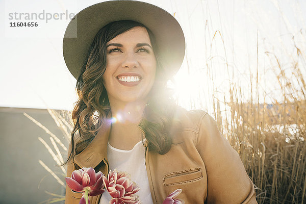 Porträt einer lächelnden gemischtrassigen Frau mit Hut und Blumen in der Hand