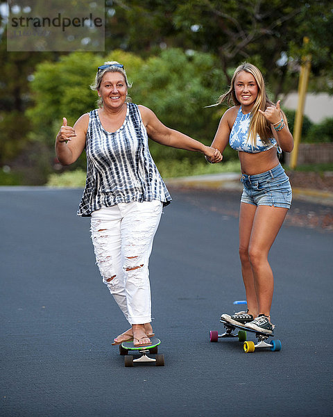 Kaukasische Mutter und Tochter halten sich beim Skateboardfahren an den Händen