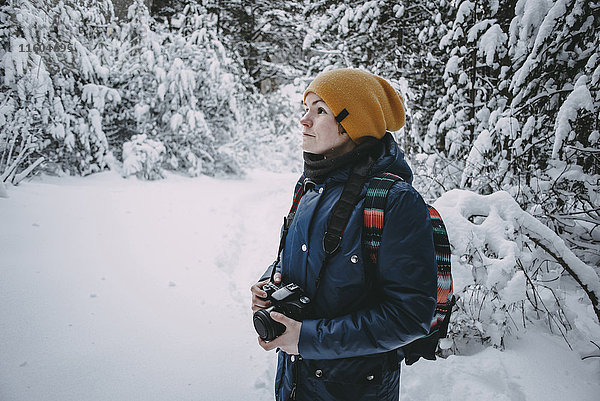 Kaukasische Frau hält Kamera im verschneiten Wald