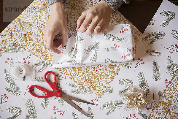 Hände einer kaukasischen Frau beim Einpacken von Weihnachtsgeschenken