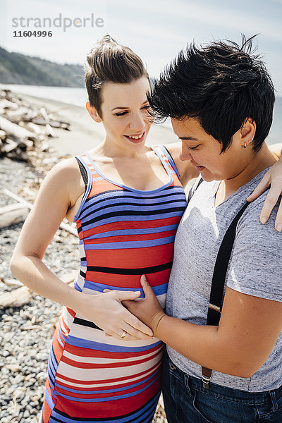 Schwangeres lesbisches Paar umarmt sich am Strand