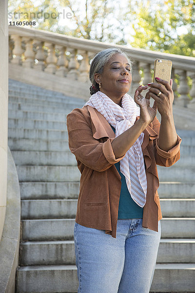Schwarze Frau auf Steintreppe  die eine SMS auf ihrem Handy schreibt
